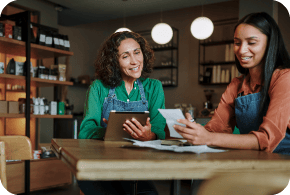 Two business women sitting at a table looking at a tablet.